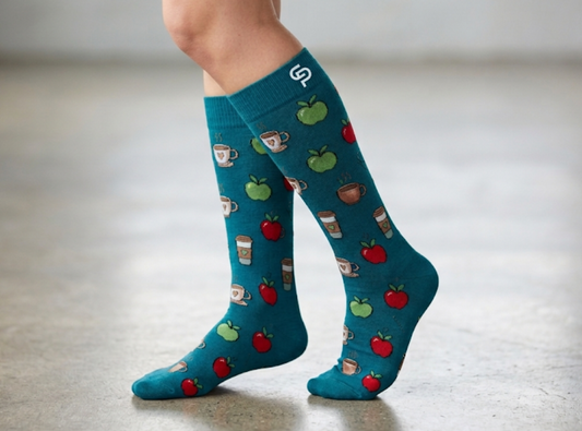Teal knee-high socks with coffee and apple pattern worn by a person on a light wooden floor.