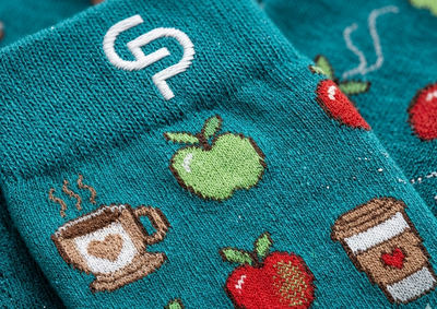 Teal socks with coffee cup, apple, and heart designs on a textured background