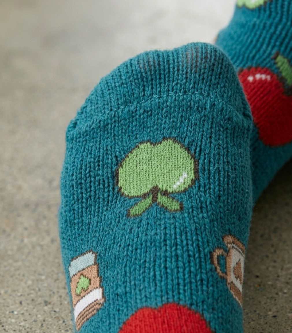 Teal sock with cartoonish apple design on a concrete surface